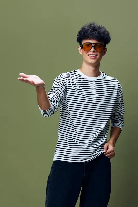 young man wearing striped shirt and sunglasses gesturing with hand, smiling confidently against green background in casual style
