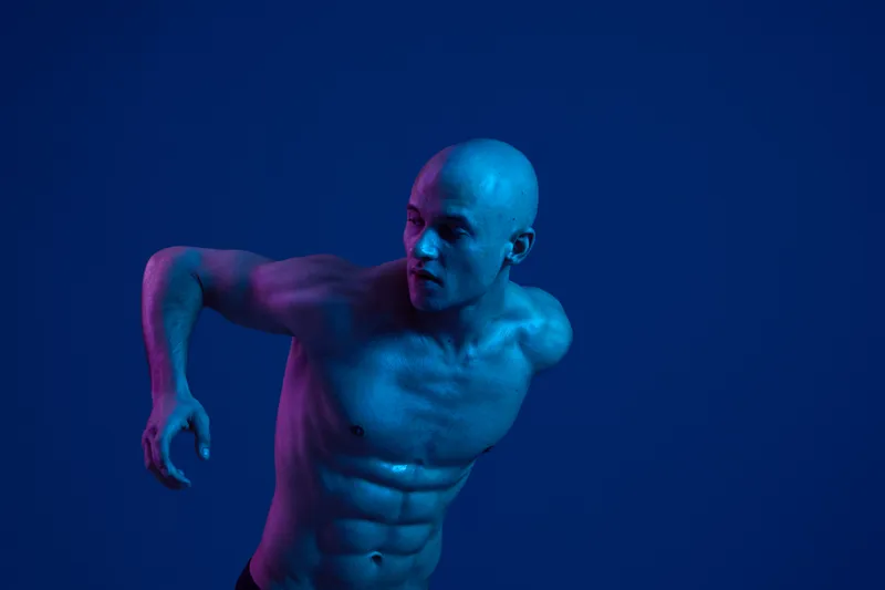 Focused man in motion, showcasing athleticism and strength, with vibrant blue lighting creating a dynamic feel in this color image.