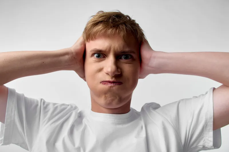 Headache and stress expression from a man pressing his temples with a grimace, conveying tension, discomfort, and frustration in a studio setting and plain background