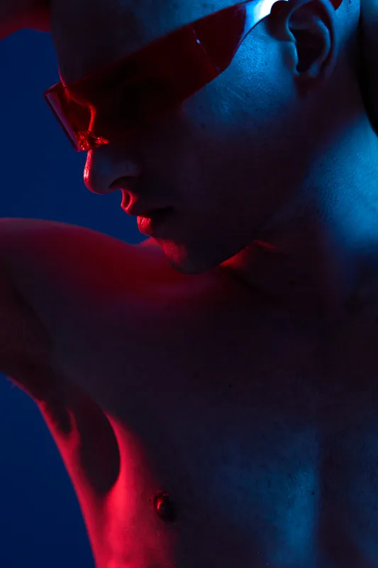 A striking portrait of a man with red-tinted glasses, showcasing an artistic interplay of light and shadow in vibrant hues. Captivating and engaging.