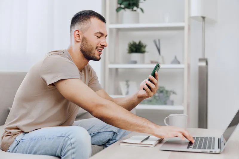 Smiling man engaging in a digital detox while balancing work tasks at home, reflecting on his emotional well-being and career choices amid modern pressures.