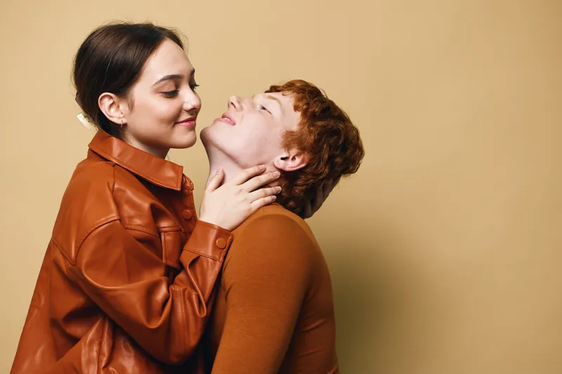 Couple, love and affection with woman embracing man showing tenderness and intimacy in warm clothing against beige background. Romantic relationship with emotional connection and care.