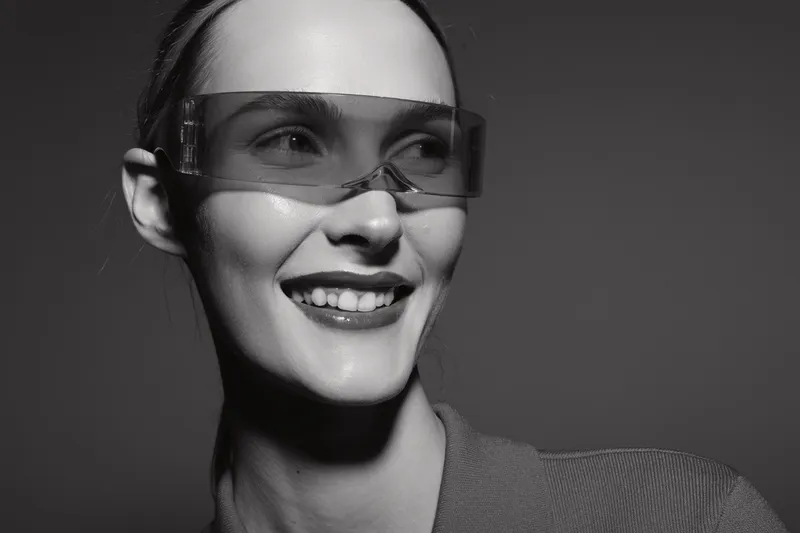 Smiling caucasian woman with light skin wearing transparent protective glasses looks away on dark background. Concept of safety, technology, and happiness.