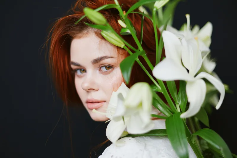 Portrait of a young woman with red hair and white lilies, expressing tranquility and beauty against a dark background