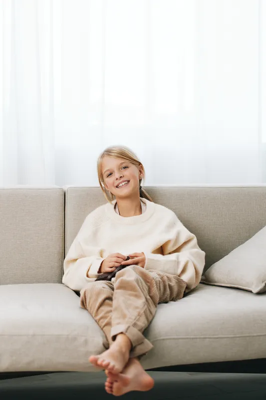 Authentic lifestyle scene featuring a smiling child on a sofa, relaxed and curious, capturing playful moments and school related activities in a cozy home setting.