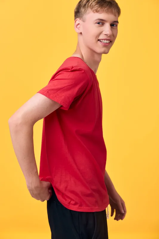 Man in casual red shirt smiles in a studio setting, posing against a vibrant yellow background. Contemporary fashion mood with bright color contrast, clean lines, and confident upbeat attitude.