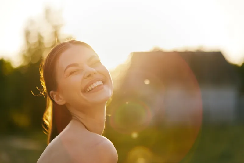 Happy young woman enjoying a sunny day outdoors, with a radiant smile and natural sunlight creating a warm atmosphere