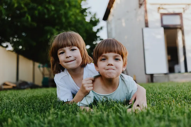 Two cheerful children playing together on green grass, showcasing joy and innocence in nature. The warm sunlight enhances the vibrant scene.