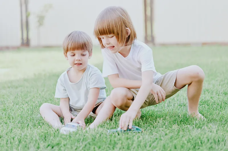 Two happy boys playing on green grass, enjoying a sunny day together while engaging in playful activities and sharing laughter outdoors.