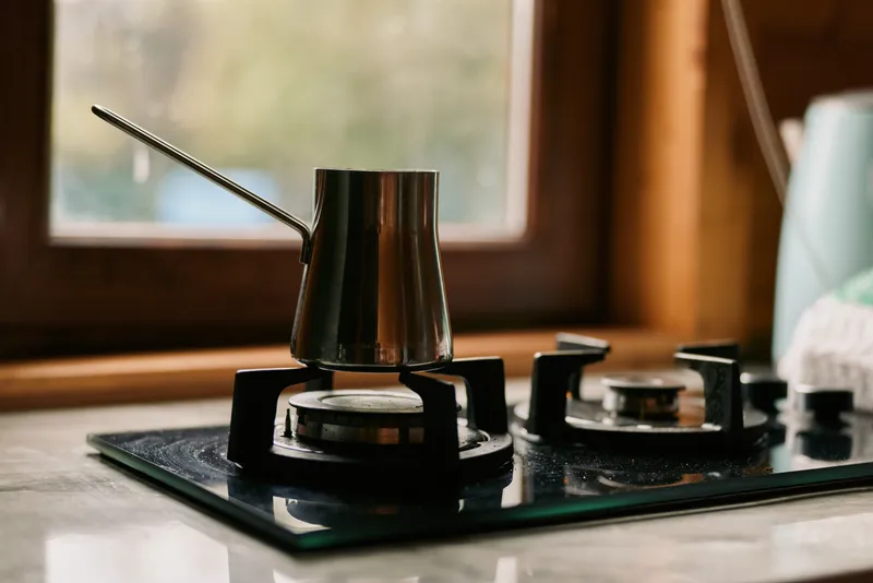 Kettle on a gas stove in a cozy kitchen, steam rising as warm light filters through a window, highlighting a simple everyday cooking moment.