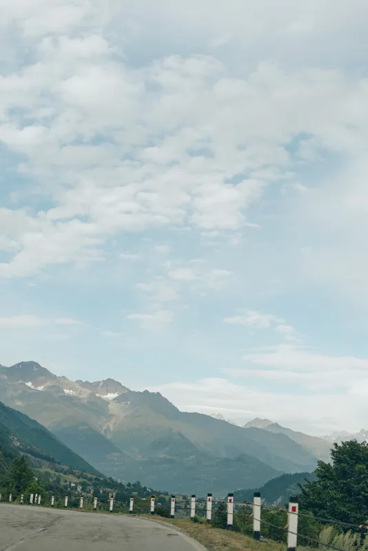 Road through rugged mountains under a blue sky with scattered clouds creating a scenic landscape ideal for travel and nature exploration and winding route through tranquil countryside for adventure