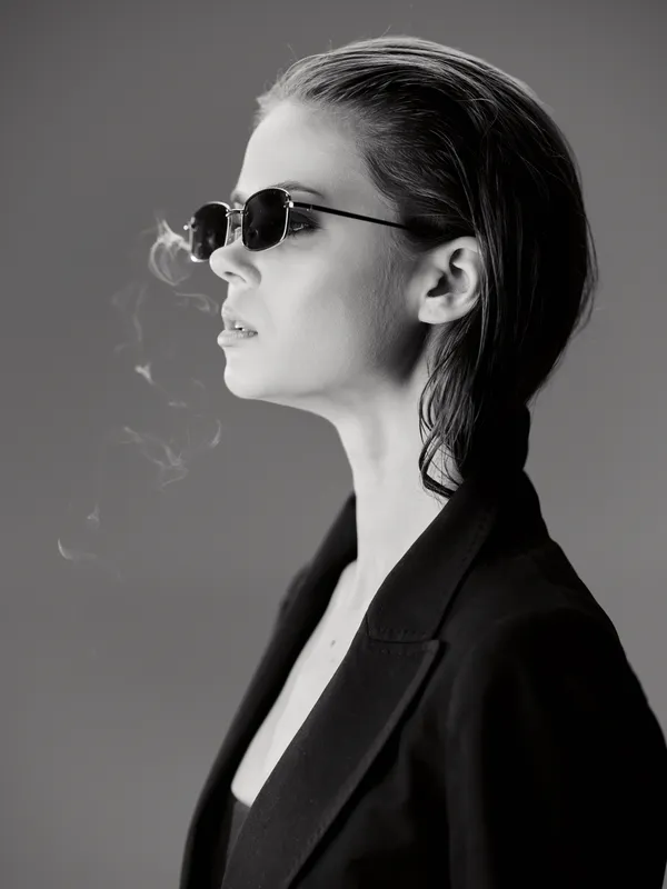 Black and white portrait of a stylish woman wearing sunglasses and smoking with a calm expression
