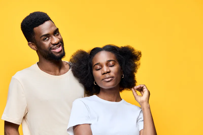 Happy young couple with natural hairstyles against a bright yellow background, representing love and positivity through vibrant colors and joyful expressions