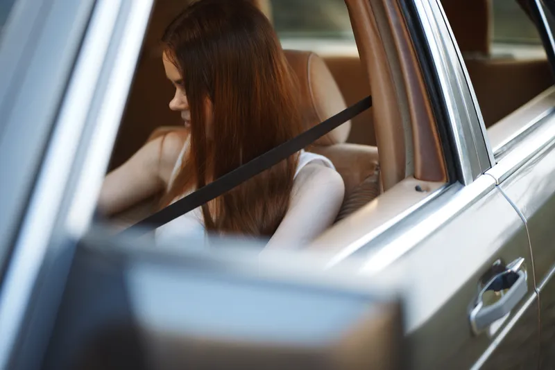Young woman with long hair sitting in a car, wearing a casual outfit, expressing a pensive emotion, ideal for concepts of travel, solitude, and introspection.