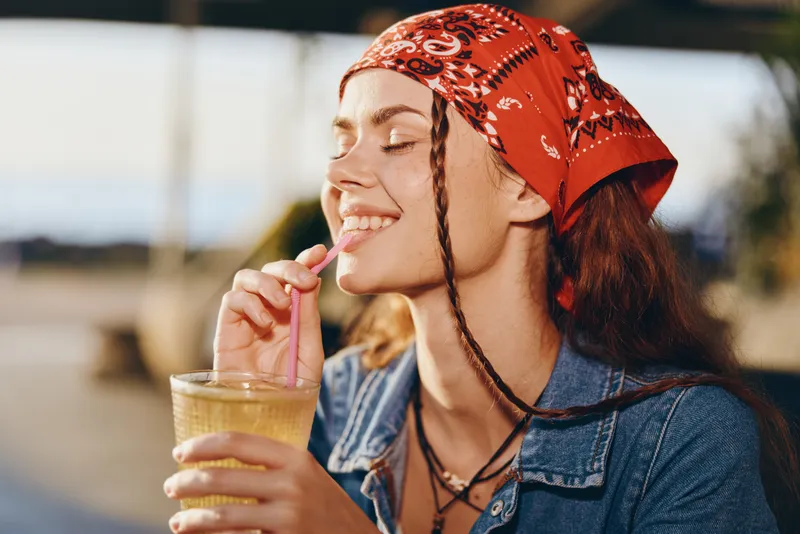 lifestyle woman enjoying drink with red bandana and denim in modern boho-western street style film color, relaxed joyful summer vibe