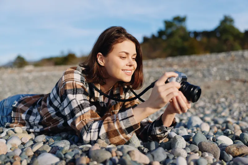 Photographer lying on pebbles at the beach, capturing moments with a camera, enjoying outdoor nature and leisure, focused and relaxed while shooting today