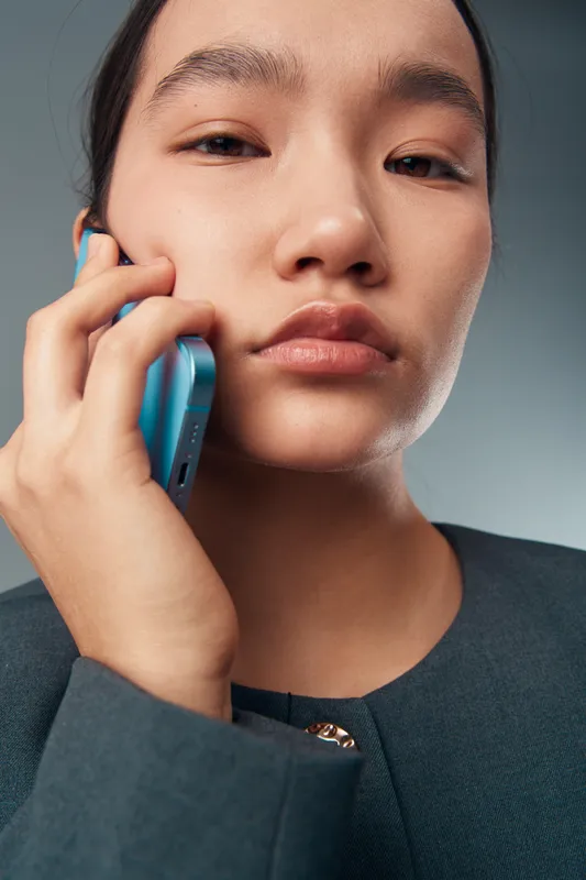Young woman talking on phone closeup portrait with focused expression indoor. Female face and hand holding smartphone, communication and technology concept with casual clothes.