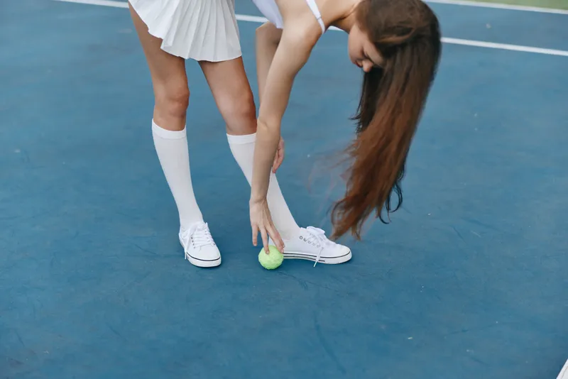 Young woman in sporty outfit picking up a tennis ball on the court, showcasing active lifestyle and motion, perfect for sports themed projects