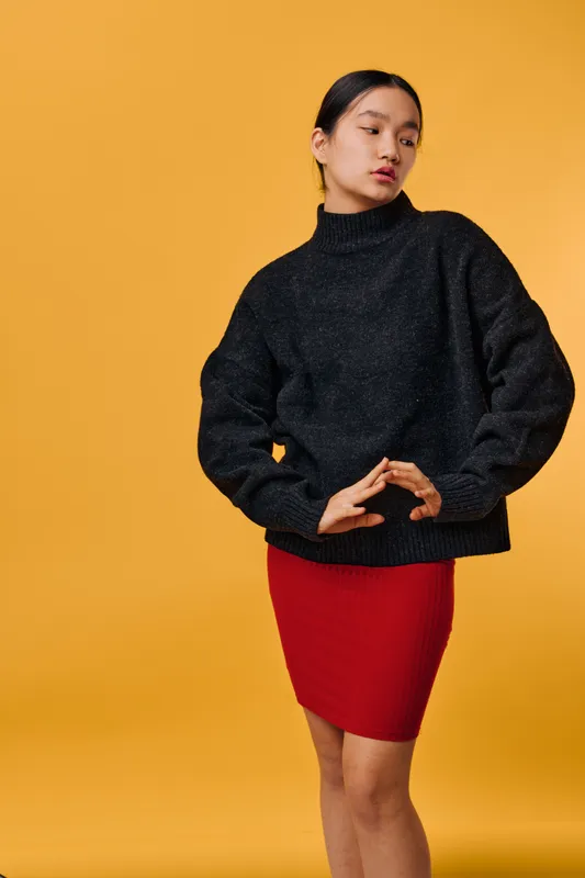 Woman, Asian, standing and posing against yellow background wearing black sweater and red skirt with casual style and confident facial expression with long hair tied back.