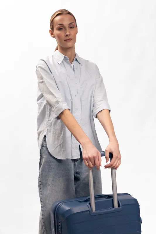 Young woman in casual clothes holding suitcase handles standing on white background. Concept of travel, tourism, and preparation for trip with luggage for vacation or business travel.