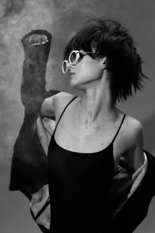black and white woman wearing sunglasses dancing with flowing jacket in studio lighting
