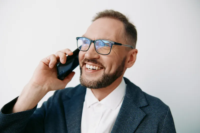 Professional businessman on a colored isolated background expresses confident joy while talking on a mobile phone, conveying success, focus, and a positive, engaging attitude.