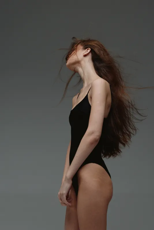 Young woman with long hair posing in black swimsuit against gray background, elegant and minimalistic style, natural beauty expression