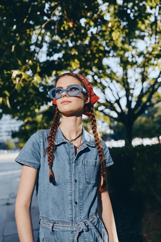 Lifestyle woman in modern boho-western denim street style with braids and sunglasses, embracing a relaxed and stylish urban look in film color tones.