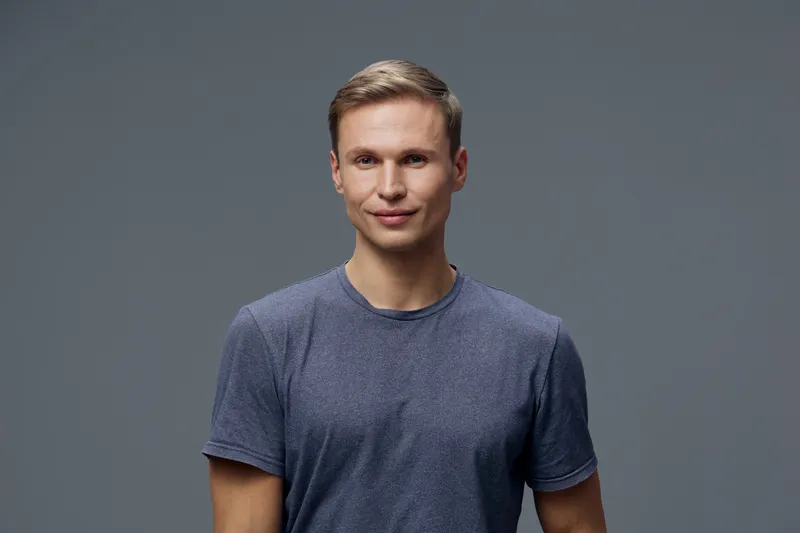 Smiling young man with short brown hair wearing casual blue t-shirt looking at camera isolated on plain gray background studio portrait. People lifestyle concept