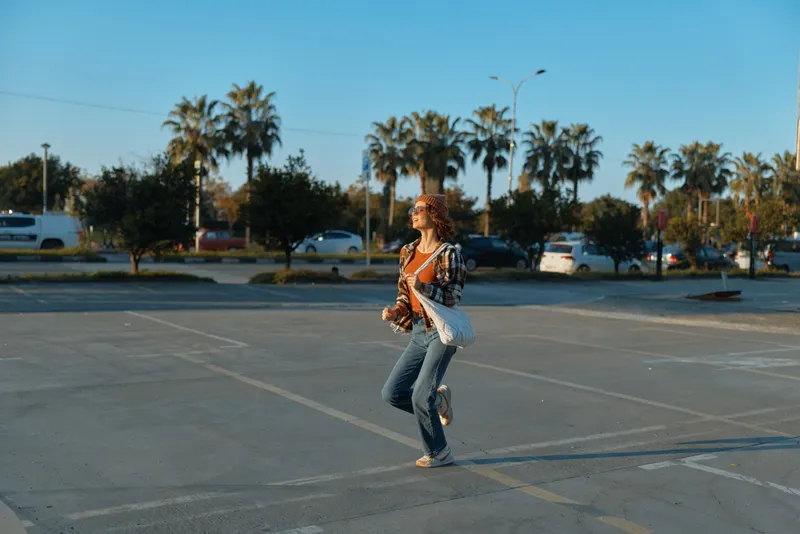 Woman walking through a sunlit parking lot by palm trees, candid lifestyle moment with golden sunlight glow, authenticity and mindful living captured in emotional storytelling.