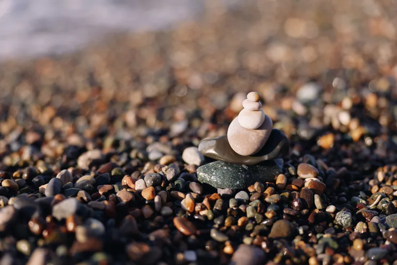 Close view of a tiny stack of smooth stones on a pebbled beach with calm water in the background, conveying balance, tranquility and focus in a natural coastal scene.