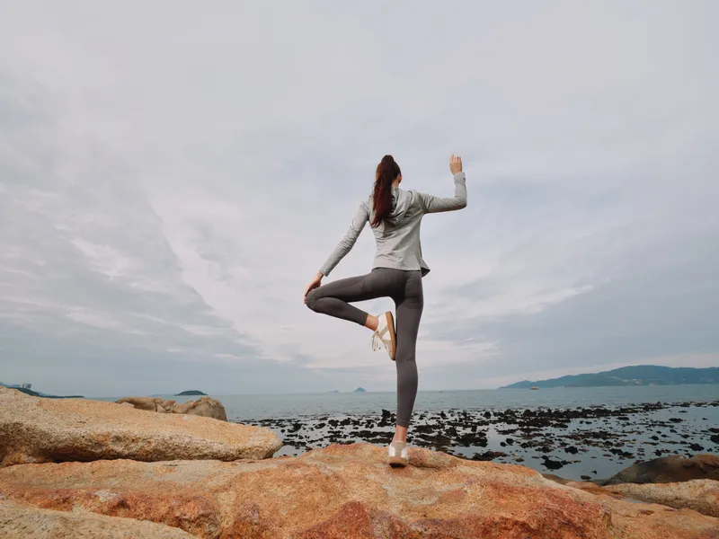 Young woman practicing yoga on rocky beach, wearing comfortable athletic apparel, enjoying peaceful ocean view and showcasing balance and tranquility in nature