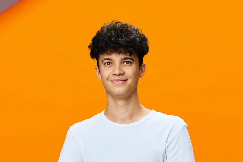 young man with curly hair wearing white t-shirt smiling against vibrant orange background, casual style, positive expression, studio lighting
