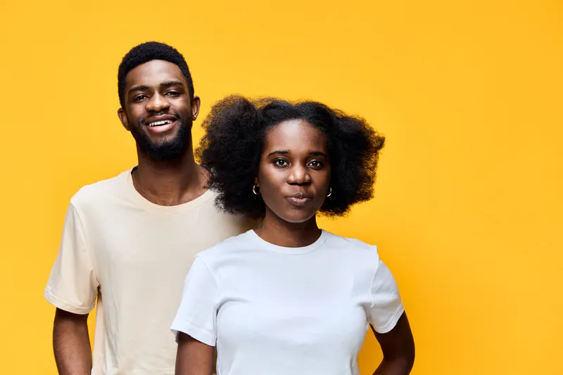 Young couple smiling together against a bright yellow background, showcasing happiness and joy through their vibrant expressions and casual attire