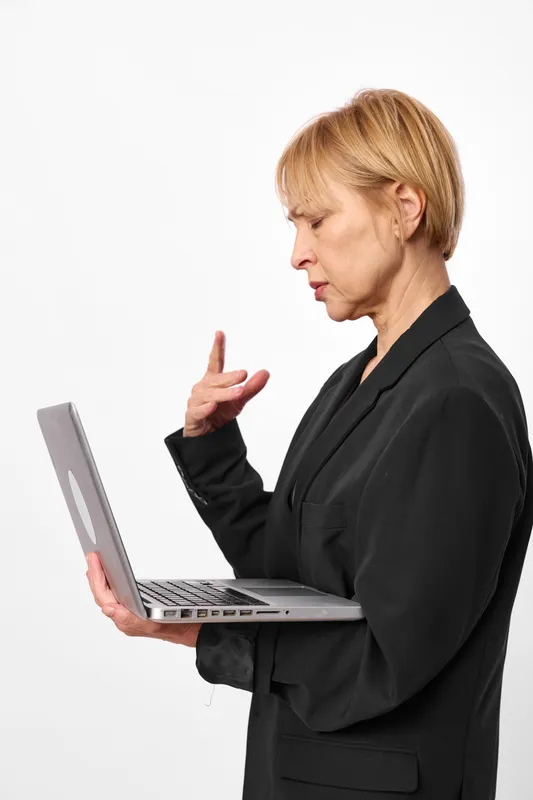 Woman with laptop, business communication gesture in a studio, focused profile, black blazer, holding notebook computer, explaining ideas, clean white background, neutral light