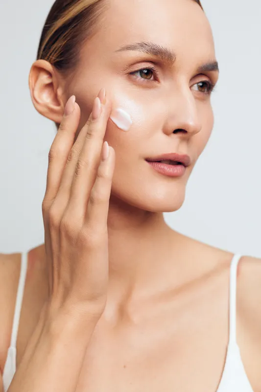 Woman skincare, applying face cream with gentle fingers, beauty and wellness routine on a clean studio background, closeup portrait, soft light, calm self care for daily hydration.
