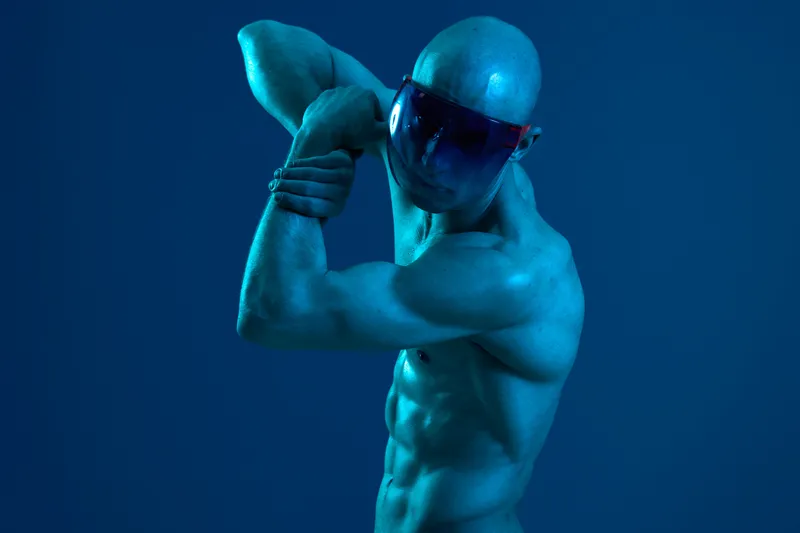 Athletic man striking a pose in vibrant blue light, showcasing his toned muscles and dynamic expression. Perfect for fitness and wellness themes.