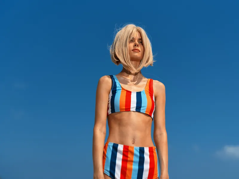 young woman in colorful striped bikini standing outdoors under clear blue sky, summer beachwear fashion, confident and relaxed pose, bright sunny day