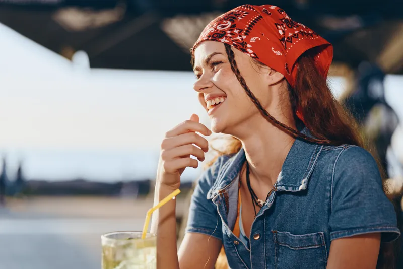 Lifestyle woman with modern boho-western denim street style smiling outdoors, wearing a red bandana, casual outfit, natural light, film color warm tones.