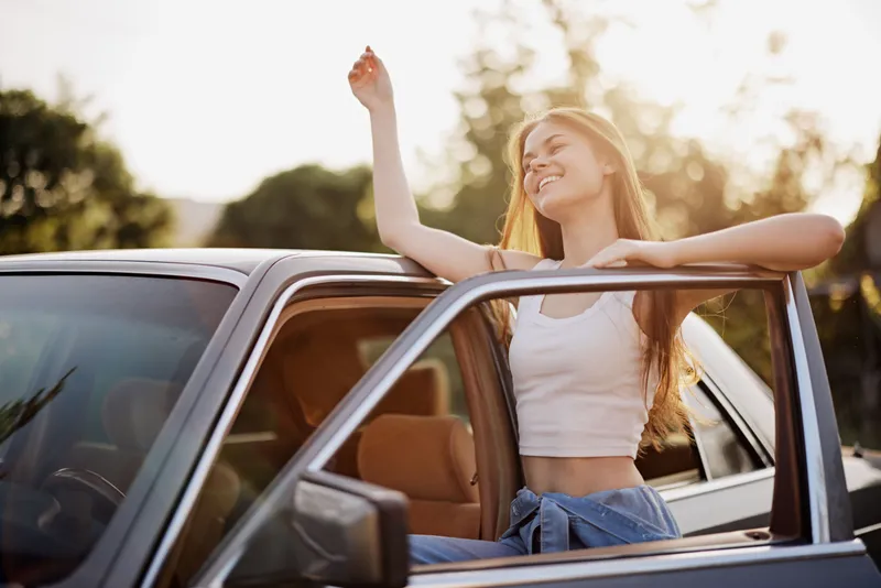 Happy woman enjoying a sunny day in a car, representing freedom and joy, wearing a casual outfit with a warm, soft color palette.
