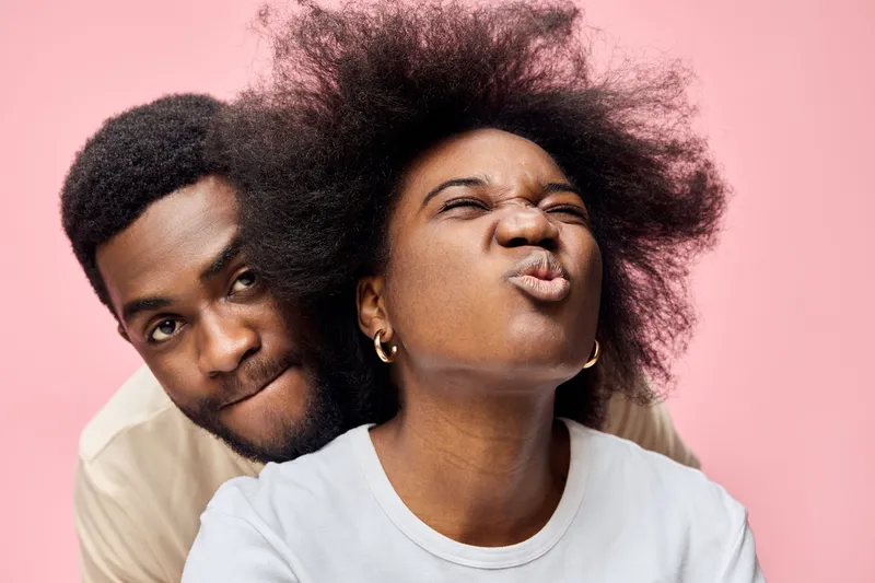 Happy couple having fun together with vibrant expressions against a soft pink background, showcasing emotional connection and joy in their relationship