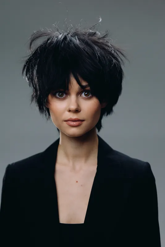 Portrait of a young woman with short black hair wearing a black blazer against a gray background