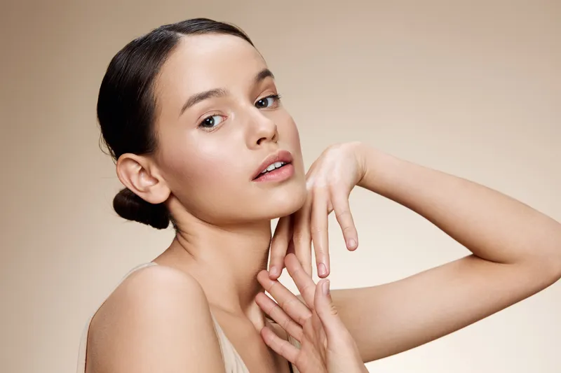 Young woman with natural makeup posing gracefully against a soft beige background, showcasing elegance, beauty, and calm emotions, ideal for health and wellness themes