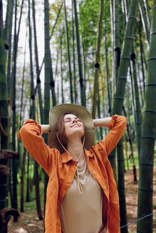 Woman in a bamboo forest wearing a hat, portrait of relaxed traveler enjoying nature and travel experience. Outdoor scene with calm expression and green vertical stems.