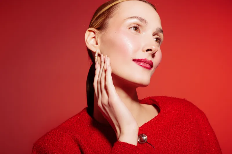 Portrait of a woman with clear skin and red lips wearing a red sweater against a red background. Concept of beauty, skincare, fashion, and confident female model in studio lighting.