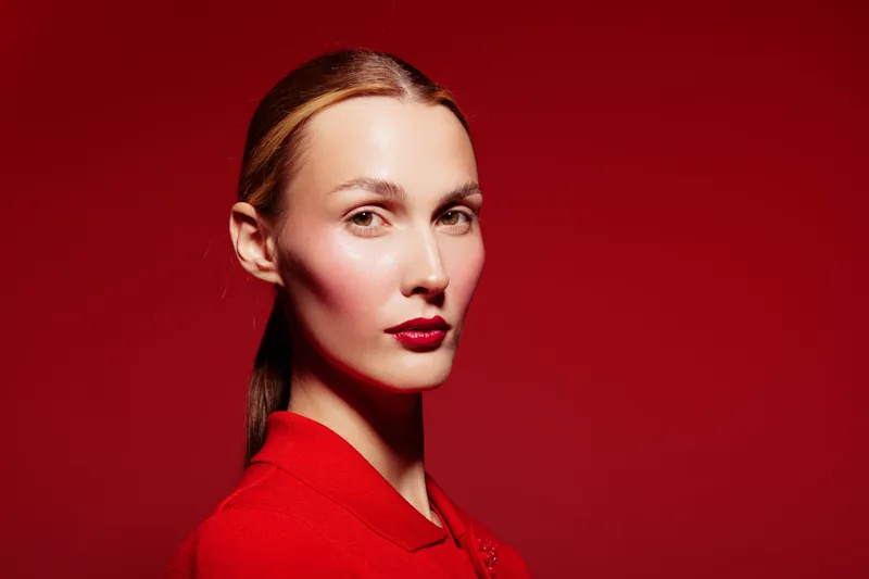 Portrait of a confident woman with red lipstick and red clothing against a red background. The image highlights beauty, fashion, and elegance with strong color contrast and lighting.