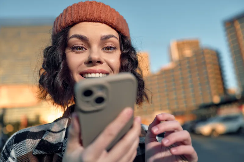 Woman with smartphone and smile in urban street at golden hour, candid moment conveying authenticity, mindful living and emotional storytelling in a modern city lifestyle.