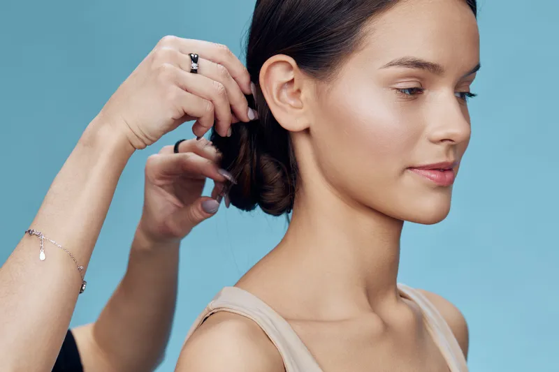 A young female model with long hair styled in a sleek bun against a soft blue background, showcasing a serene expression and minimalist fashion