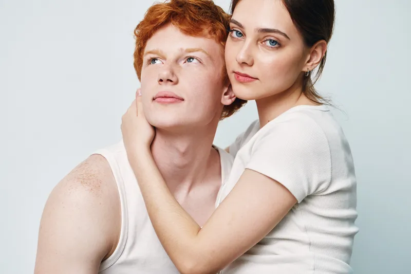 Couple, young woman and man embracing with gentle expression showing affection and closeness in studio with white background. Portrait, love, relationship and support.