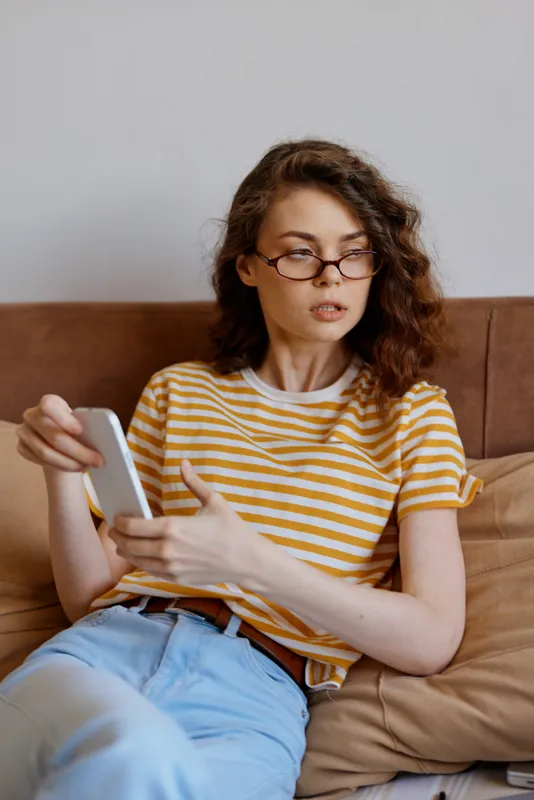 Woman relaxation indoors, casual lifestyle at home, reading on a tablet, wearing striped yellow shirt and glasses, cozy couch setting, soft natural light, calm atmosphere in a quiet living space with